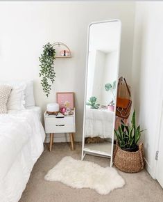 a bedroom with a white bed, mirror and plant in the corner next to it