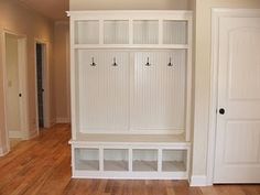 an empty room with several white shelves and doors on the wall, in front of a wooden floor