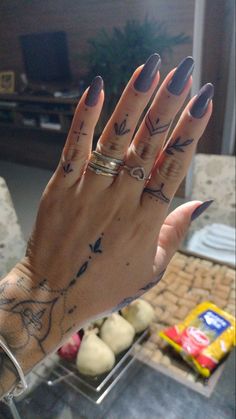 a woman's hand with tattoos and rings on her fingers, in front of a table