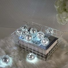 several disco balls in a wire basket with white lights on the floor next to it