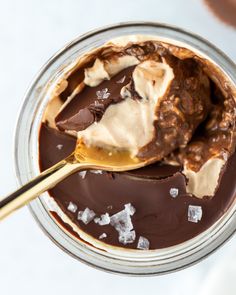 a spoon full of ice cream and chocolate in a glass bowl with some other items