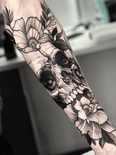 a skull with flowers on it's arm is shown in black and grey ink