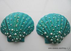 two seashells with pearls on them sitting side by side, one is green and the other is blue