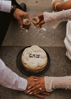 two people are toasting glasses over a cake on the ground while another person is holding a wine glass in their hand