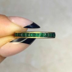 a woman's hand holding a gold ring with emeralds on it and the band