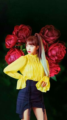 a woman with long hair wearing a yellow shirt and black skirt standing in front of red roses