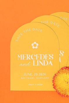 an orange save the date card with a yellow flower on it next to some cards