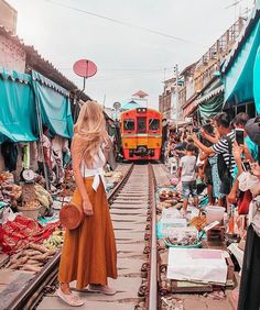 a woman is standing on the train tracks in front of an outdoor market with lots of people