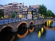 an old stone bridge over a river with lights on at night in the city center