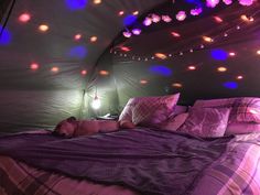 a bed in a tent with lights hanging from the ceiling and pillows on the floor