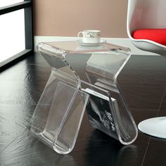 a glass table with a magazine holder on it next to a red chair and window