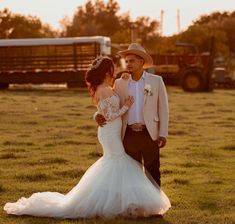 a bride and groom standing in the middle of a field at sunset with a tractor behind them