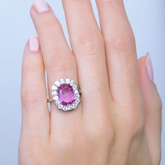 a woman's hand holding a ring with an oval shaped pink stone surrounded by diamonds