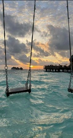 two swings in the middle of water with a pier in the background at sunset or dawn