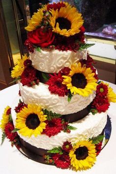 a three tiered cake with sunflowers and red flowers on the bottom layer