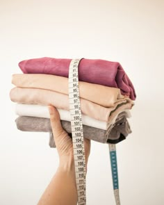 a person holding three folded shirts with a measuring tape