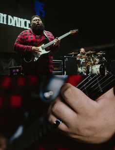 a man is playing an electric guitar on stage with other musicians in the back ground