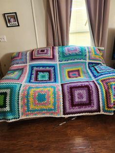 a crocheted blanket is sitting on the floor in front of a window with curtains