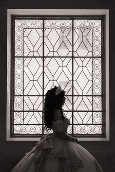 a black and white photo of a woman in a wedding dress looking out a window