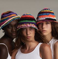 three beautiful women wearing colorful hats standing next to each other