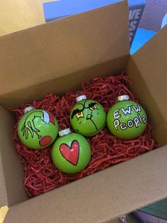 three green ornaments in a cardboard box with graffiti on them and the words slow people painted on them