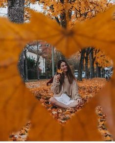 a woman sitting on the ground in front of a heart shaped frame with leaves around her