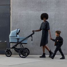 a woman pushing a stroller with a young boy walking beside her on the sidewalk