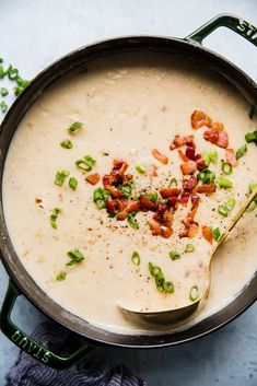 a pot full of soup with bacon and green onions on the side, ready to be eaten