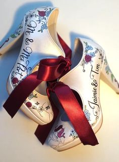 two pairs of white shoes with red ribbon tied around the bottom one shoe has an inscription on it