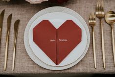 the place setting is set with two heart shaped napkins, gold forks and silverware