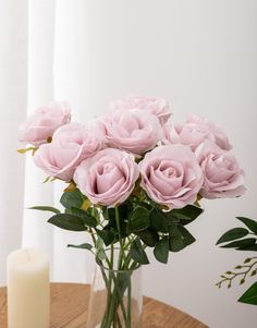 a vase filled with pink roses sitting on top of a table next to a candle