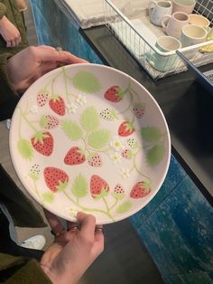 a person holding a plate with strawberries painted on it and other plates in the background