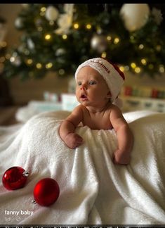 a baby laying on top of a blanket next to a christmas tree