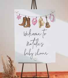 a welcome sign is hanging on a clothes line with boots and baby shower items in the background