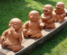 five little buddha statues sitting on top of a wooden bench in the grass with their mouths open