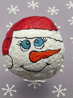 a painted rock with snowflakes on it and a santa claus face in the middle