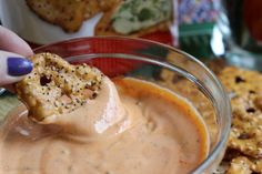 a person dipping some crackers into a bowl of dip with other snacks in the background