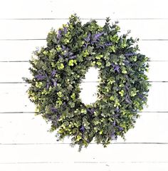 a green wreath with purple flowers hanging on a white wooden wall in the shape of a letter o