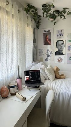 a laptop computer sitting on top of a white desk next to a bed covered in pictures