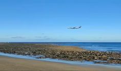 an airplane is flying low over the water and rocks on the beach near the ocean