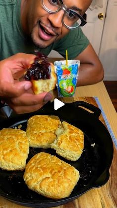 a man is holding up some biscuits and jam in front of him while he eats them