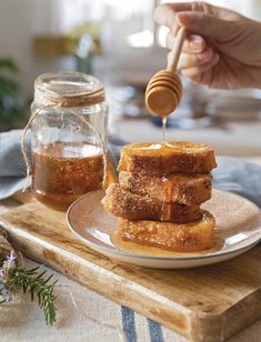 honey being drizzled on to pieces of bread sitting on a plate next to a jar of honey