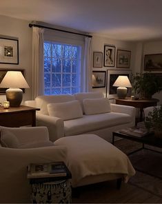 a living room with couches, lamps and pictures on the wall in front of a window