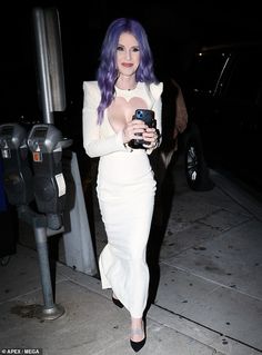 a woman with purple hair walking down the street holding a cell phone in her hand