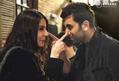 a man and woman standing next to each other in front of a brick wall talking