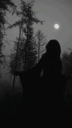 a person standing in the dark with their arms spread out and trees behind them, looking at the moon