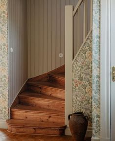 a vase sitting on top of a wooden floor next to a set of stairs in a house