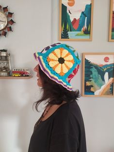 a woman wearing a crocheted hat standing in front of pictures on the wall