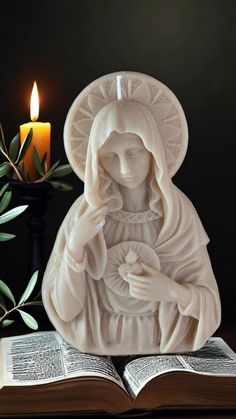 an open book sitting next to a candle and statue