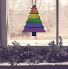 a stained glass christmas tree sitting on top of a window sill next to pine cones